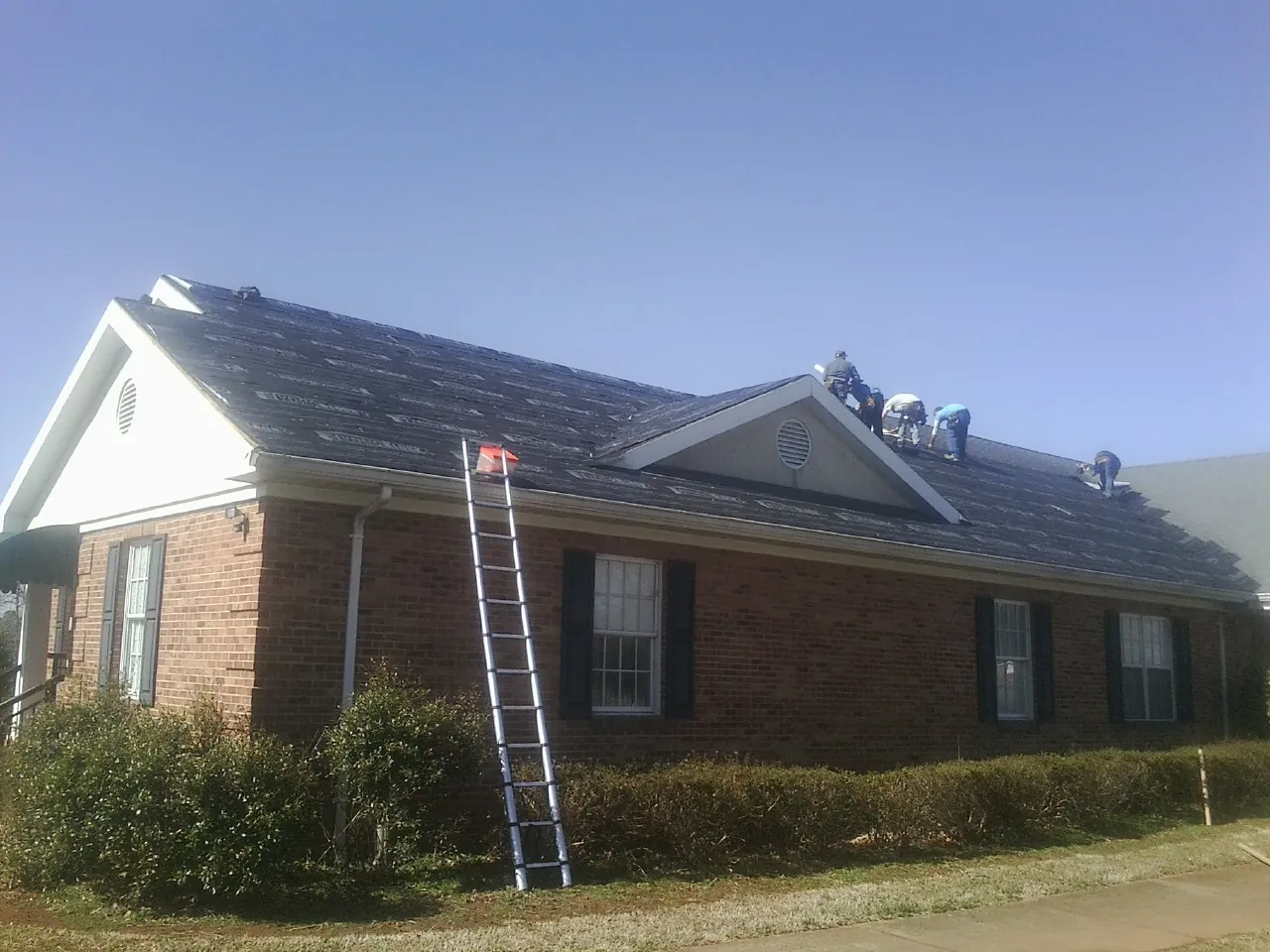 Crew tearing shingles off a brick ranch roof with a ladder set — Metal Roof Repair work by our crew in Rowesville