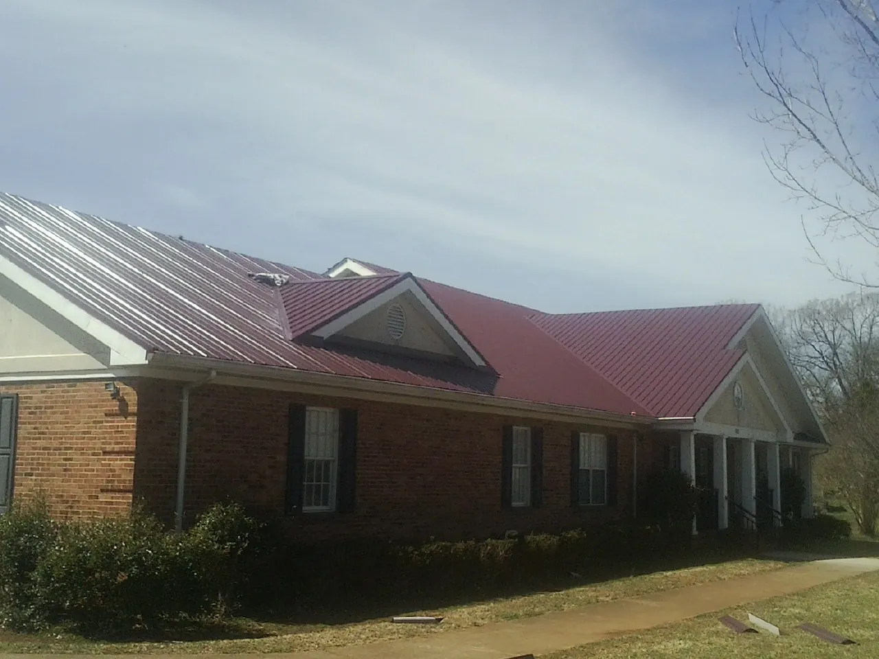 Red metal roof with gabled entries on a long brick building, from a Hail Damage Roof Repair job in Rowesville
