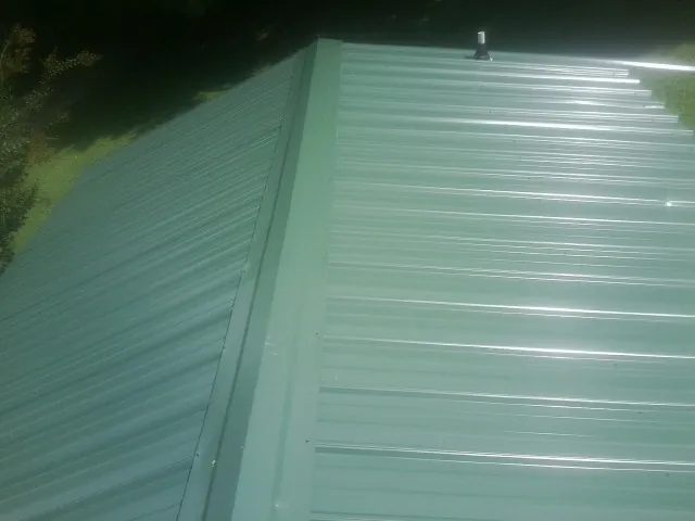 New green metal panels meeting at the ridge of a roof — Flat Roof Repair work by our crew in Rowesville