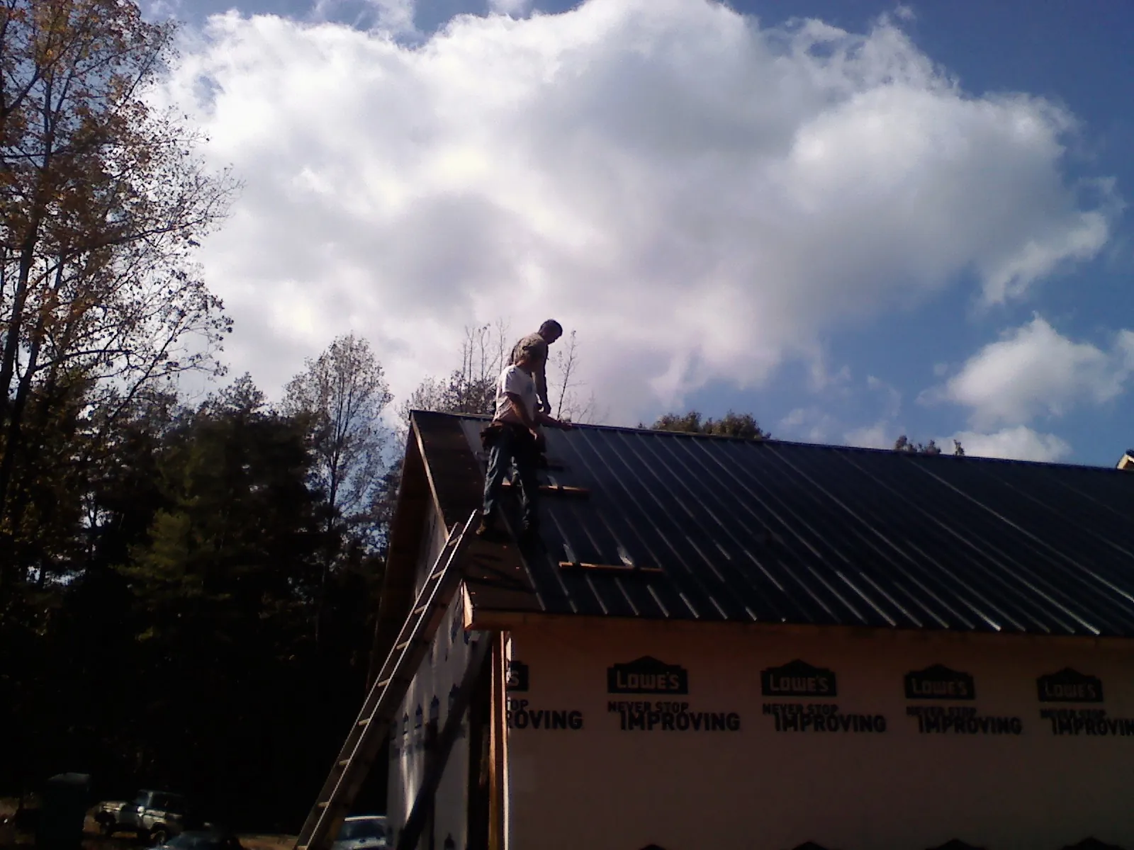 Roofer fastening dark metal panels high against a cloudy sky, from a Roof Inspection job in Rowesville